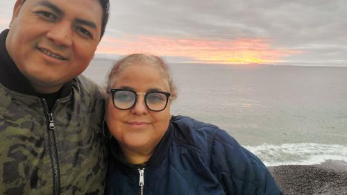 Photo of Luis Asencio Cordero and Sandra Munoz, whose case regarding due process rights for spouses in mixed-status marriages is before the U.S. Supreme Court. Luis has his arm around Sandra and both are smiling at the camera. Behind them the sun is setting over a body of water.