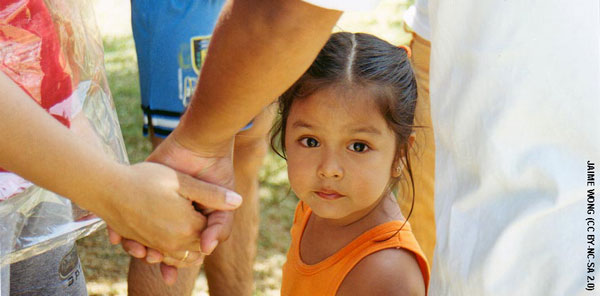 Child looking at camera with serious look on her face as her parents hold hands next to her.