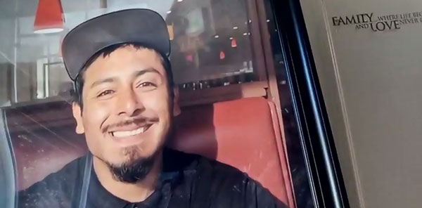 Screenshot of a close-up video image of a portrait of Victor, who is wearing a black shirt and baseball cap and a goatee, and smiling widely at the camera.