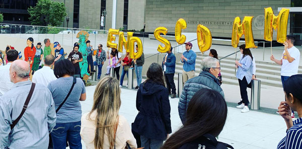 Photo of a group of protesters outside a federal court building, some holding gold-colored balloons spelling out "End S-Comm."