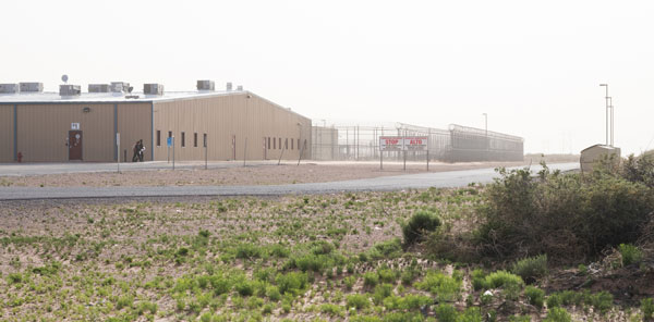 Photo of the outside of Otero Detetnion Center: a prison with fencing and barbed wire surrounded by desert sand and scrub