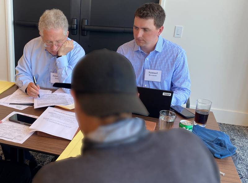 Two attorneys work on paperwork while sitting across from their client, whose back is facing the camera.