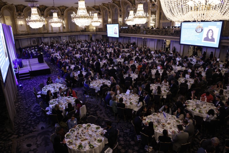 View looking down from a balcony on an elegant and ornate ballroom filled with people sitting at round tables.