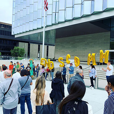 Photo of an End S-comm rally in May 2019 outside the courthouse during the trial in Gonzalez v. ICE. Protesters are gathered holding balloons which spell out S C O M M