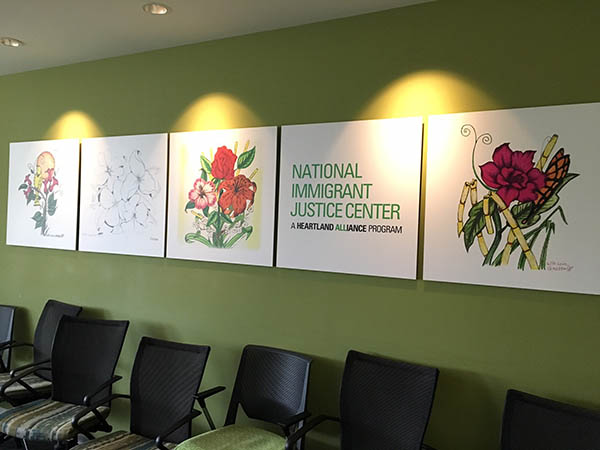 Four large panels of art, with colorful drawings of flowers and bamboo on them, hang on a wall in an office.