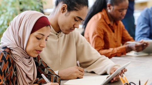 Photo of three people sitting on one side of a table doing paperwork.