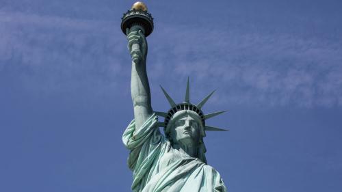Photo of the torso, head and raised arm of the Statue of Liberty, with a clear blue sky in the background