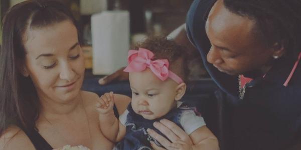 A mother holds a baby on her lap while the father looks down adoringly.