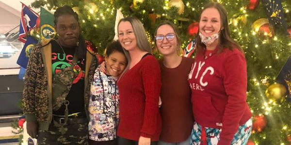 Kenault poses in front of a giant airport Christmas tree with his arm around his daughter, wife, and other family members, who are all smiling as they welcome him home to Virginia.
