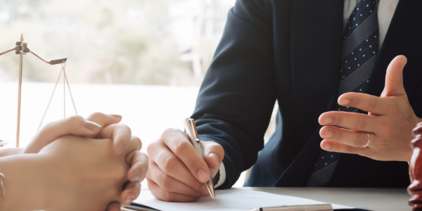 Photo of two people's hands, one person is wearing a suit and is writing with a pen on a notepad