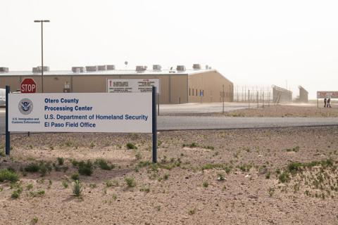 A photo of the outside of Otero Service Processing Center - a prison surrounded by desert sand and scrub bushes