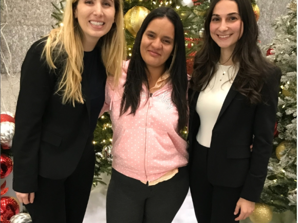 A mother from Honduras who recently won asylum poses with members of her legal team for a photo in front of festive holiday decorations.