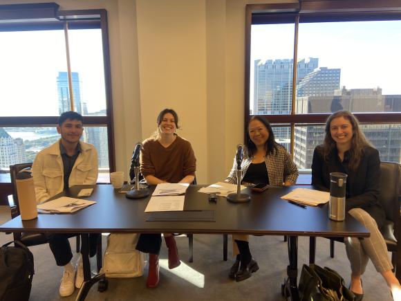  Four professionals sitting at a conference table, smiling in a well-lit office in Winston & Strawn LLP with a cityscape visible through large windows in the background.