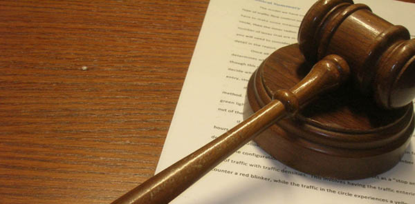 Photo of a gavel resting on a sheet of paper on top of a wood desktop