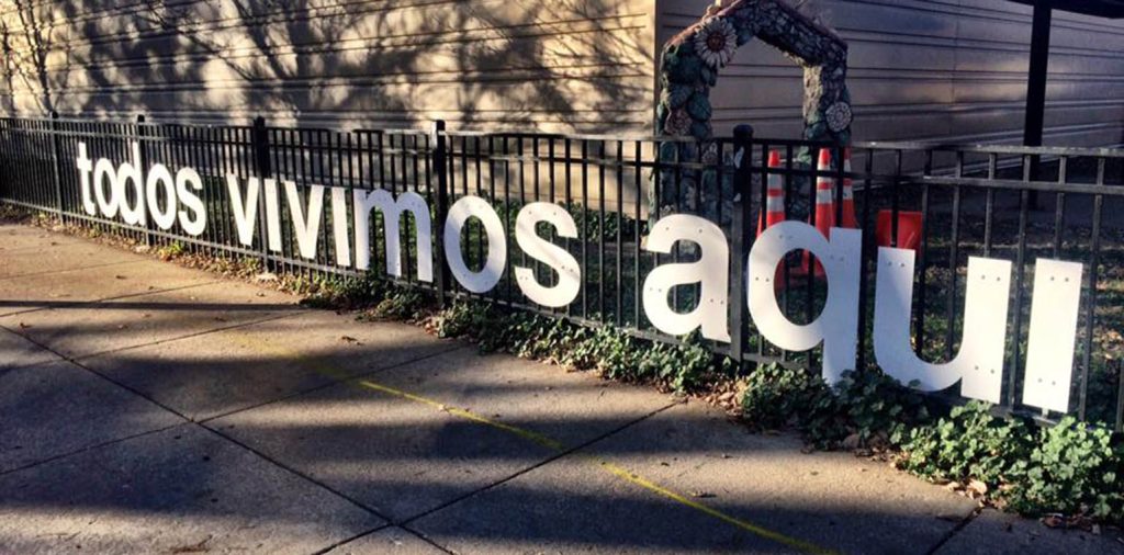 Large white letters line the fence of a school saying, "todos vivimos aqui"