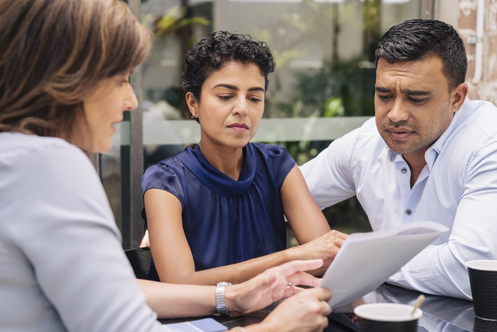 A couple and their legal advocate sit at a table, all three reviewing the same printed document.