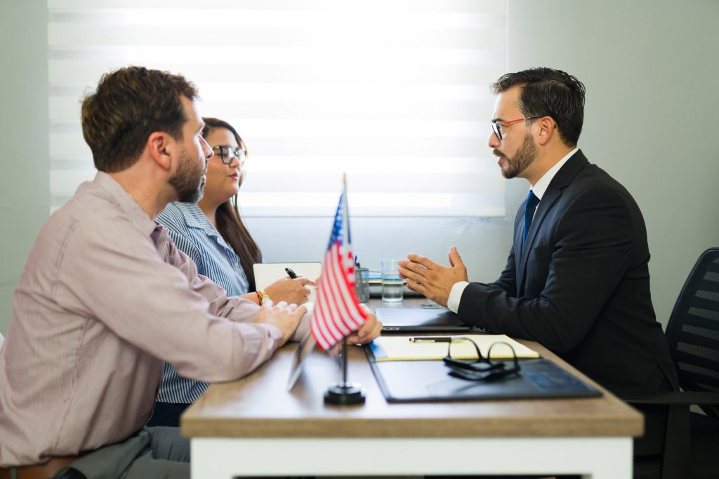 A couple meet with an immigration attorney. A small U.S. flag sits in the foreground on the desktop between them.